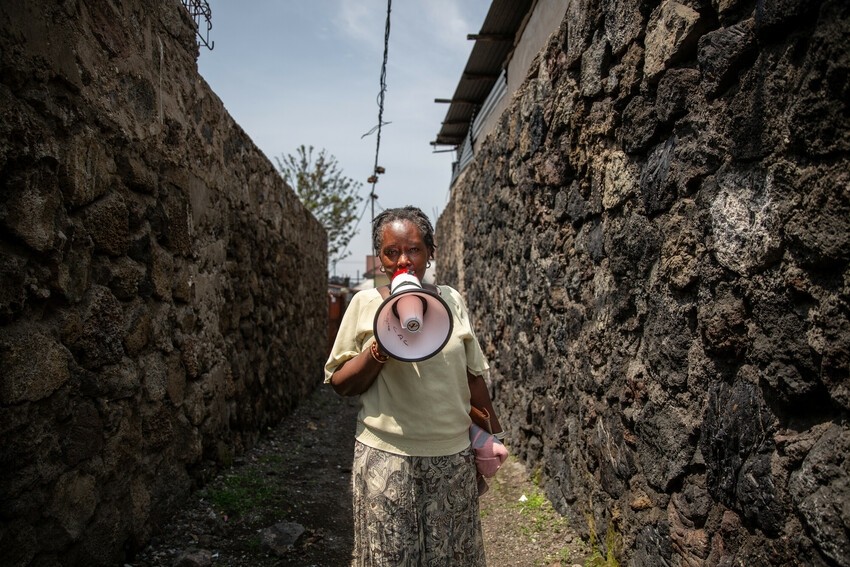 Woman walks through her community with megaphone, informing people of immunizations and other health services available.