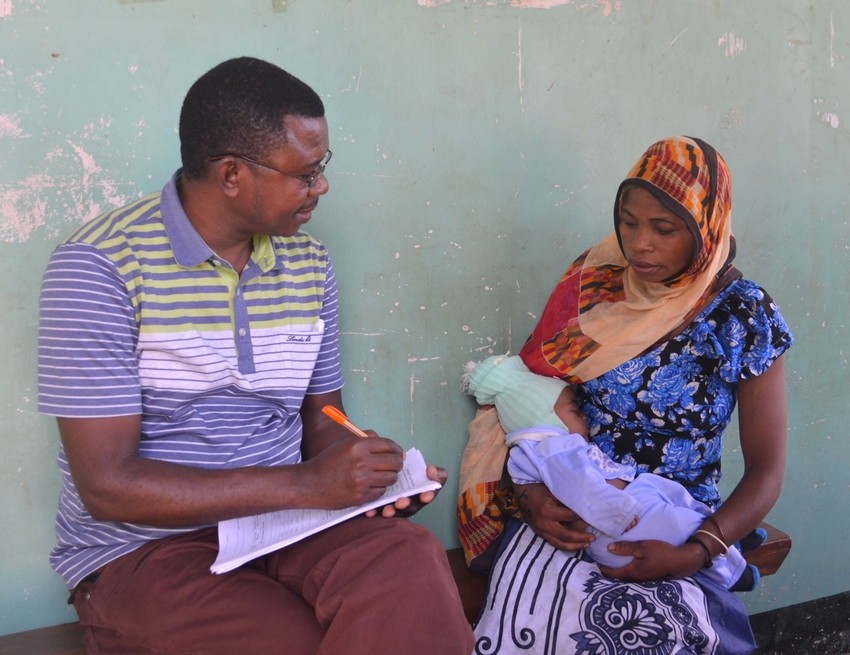 A man takes notes on a sheet of paper and sits next to a woman holding an infant