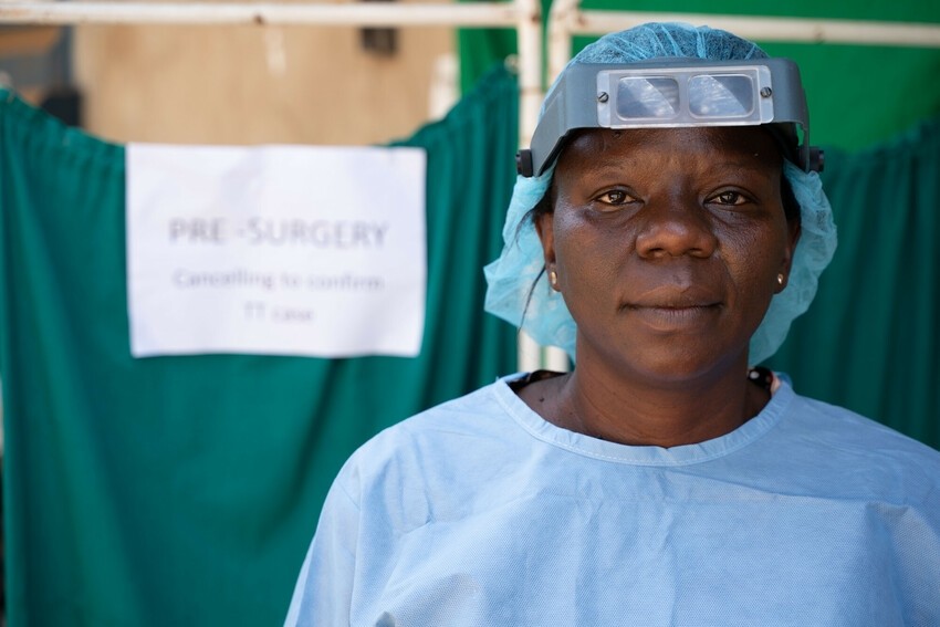 A nurse in scrubs stands in front of a surgical screen